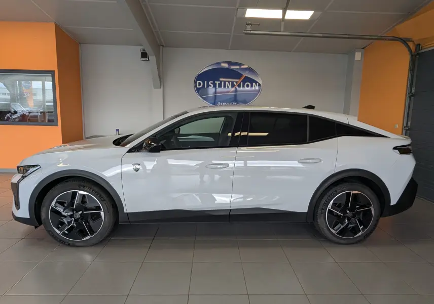 Vue latérale droite d'une Peugeot 408 Hybrid 145 e-DCS6 GT blanche Okenite avec jantes alliage 19 pouces bicolores en intérieur showroom.