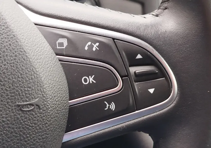 Gros plan sur les commandes multifonctions noires du volant en cuir de la Renault Mégane gris Titanium, version 2018.