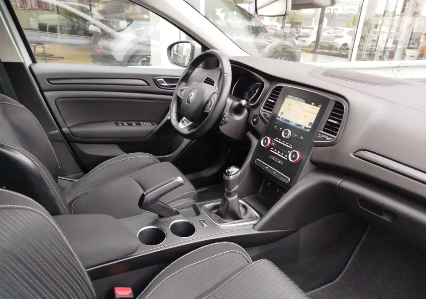 Vue intérieure côté conducteur de la Renault Mégane gris Titanium, montrant le tableau de bord et la console centrale avec boîte manuelle.