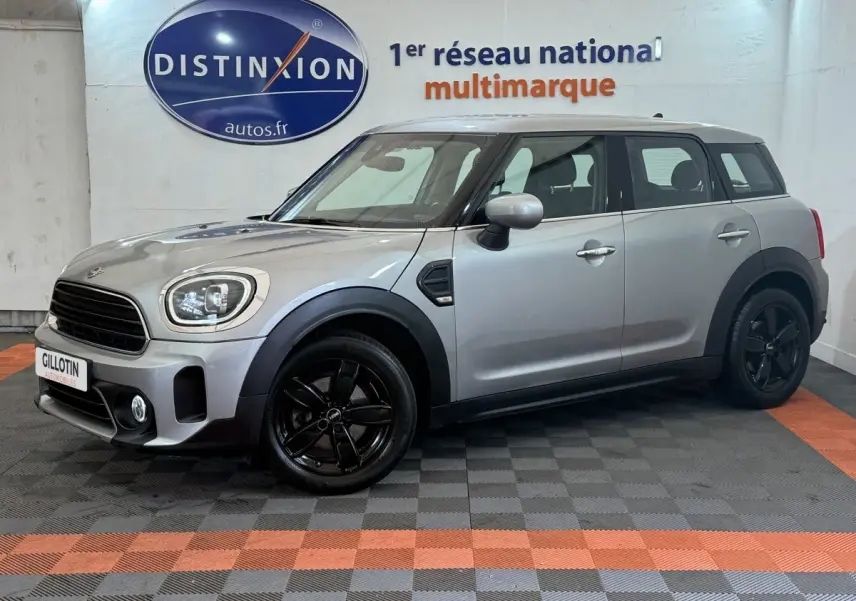 Vue de profil droit d'une MINI Countryman Cooper Essential gris clair avec jantes noires, stationnée en intérieur showroom.