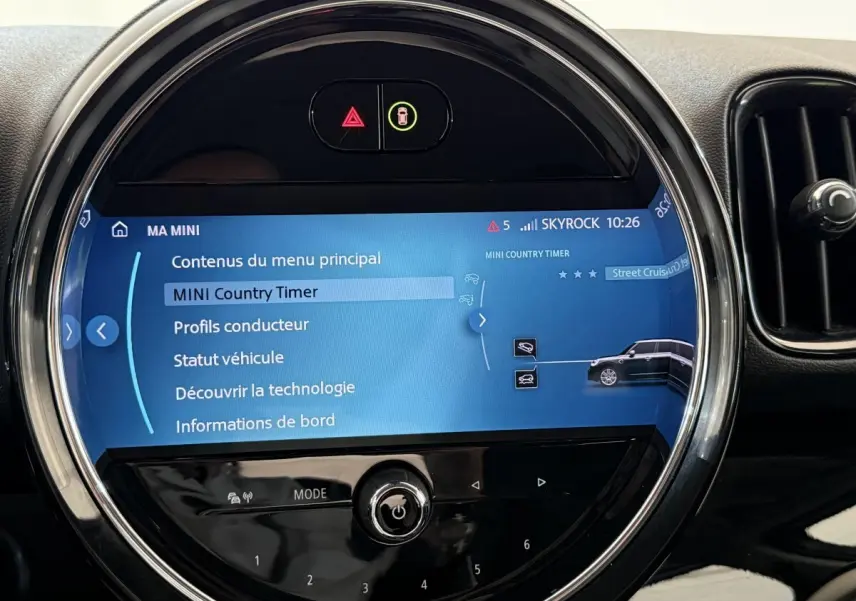 Vue rapprochée de l’écran tactile rond du tableau de bord d’une MINI Countryman gris clair, affichant le menu principal.