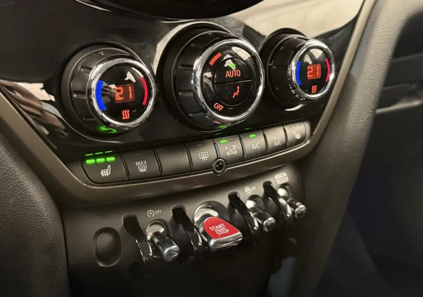 Gros plan sur les commandes de climatisation et le bouton start/stop rouge du tableau de bord noir du MINI Countryman gris clair.