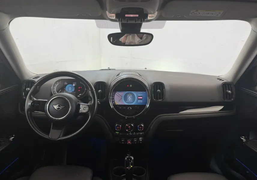 Vue intérieure frontale du tableau de bord noir et volant cuir d’une MINI Countryman gris clair 2023 avec écran tactile central rond allumé.