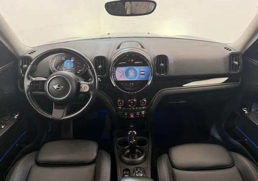 Vue intérieure frontale du tableau de bord noir et volant cuir du MINI Countryman gris clair 2023 avec écran tactile central rond.