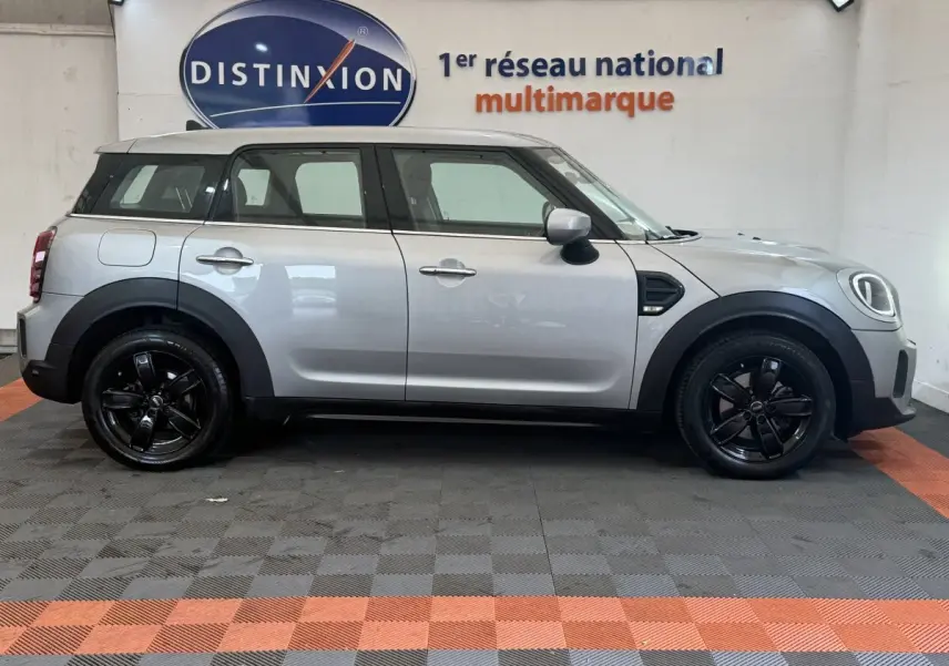 Vue de profil côté gauche d'une MINI Countryman Cooper Essential gris clair avec jantes noires, stationnée en intérieur.