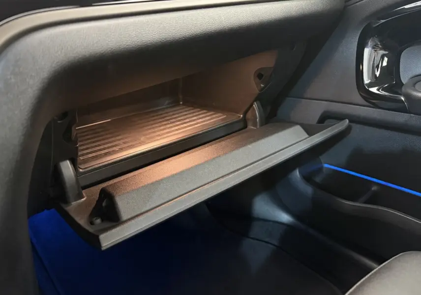 Gros plan sur la boîte à gants ouverte côté passager du MINI Countryman 2023 avec éclairage d'ambiance bleu.