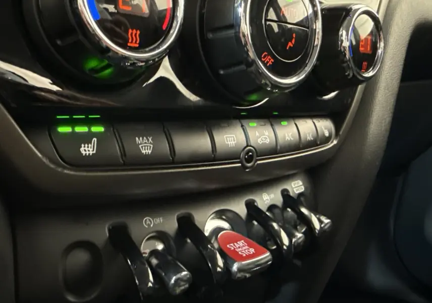 Gros plan sur la console centrale du MINI Countryman gris clair 2023, avec boutons de climatisation et bouton start/stop rouge.