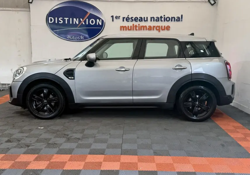 Vue de profil côté gauche d'une MINI Countryman Cooper Essential gris clair avec jantes noires dans un showroom.