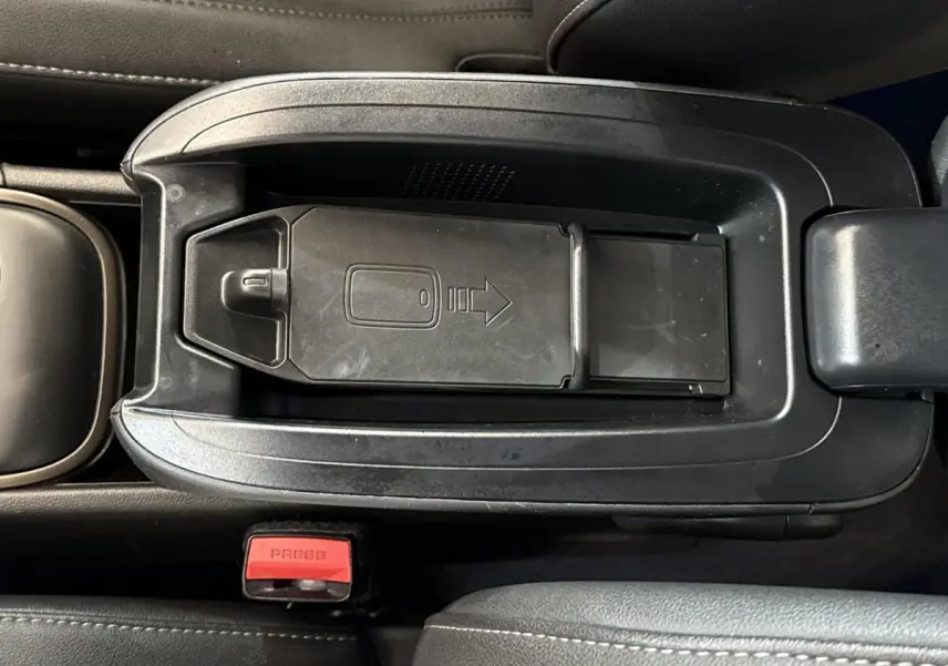 Vue rapprochée du rangement central noir avec porte coulissante et bouton de ceinture rouge dans le MINI Countryman gris clair.