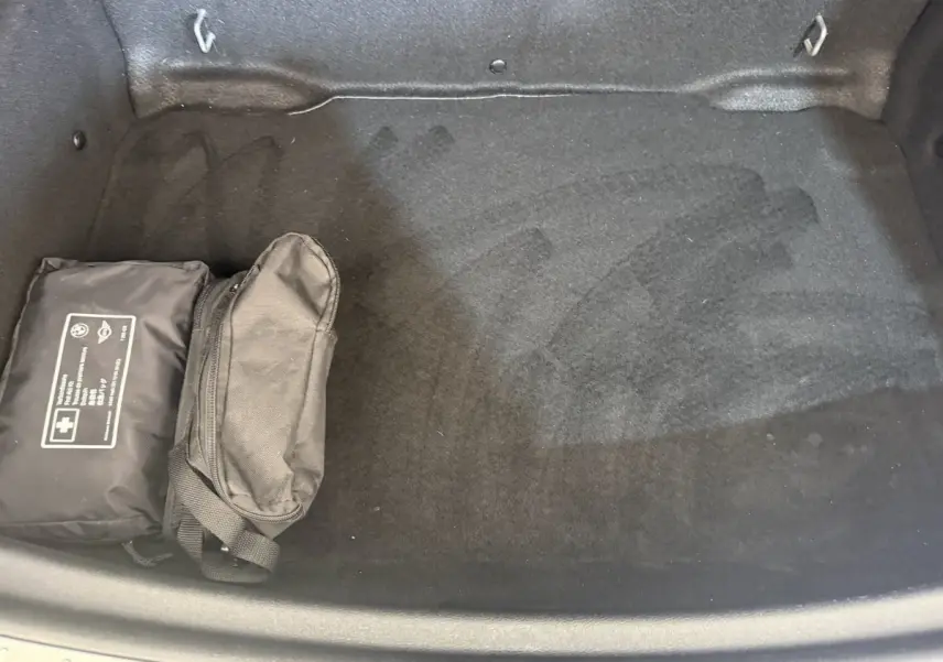 Coffre ouvert d’une MINI Countryman gris clair, vue plongeante montrant un tapis noir et deux trousses noires rangées à gauche.
