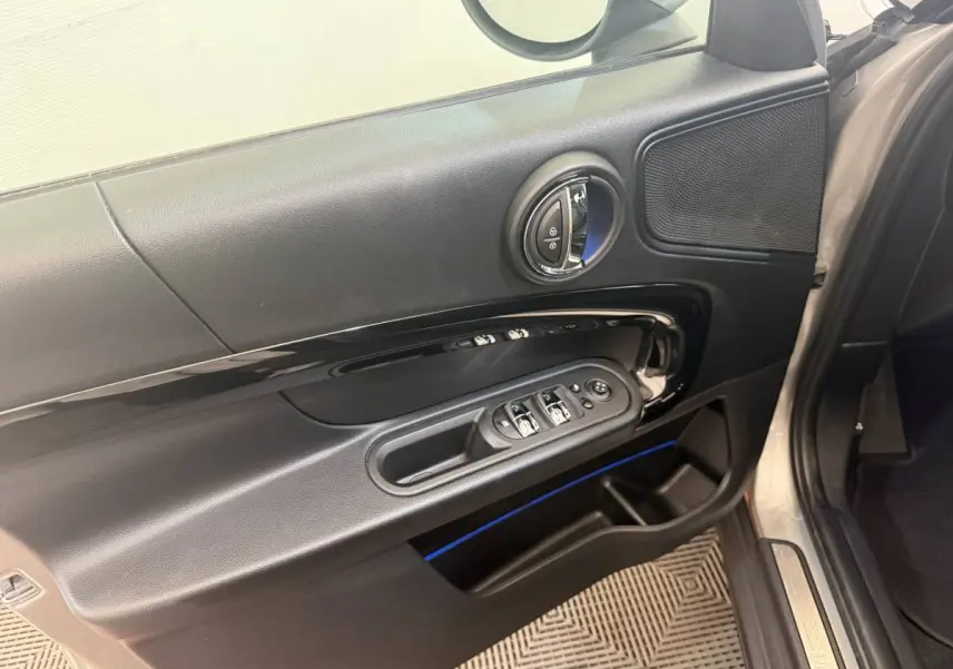 Détail de la porte avant gauche d’une MINI Countryman gris clair, montrant les commandes des vitres et le haut-parleur.