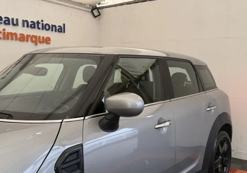Vue de côté droit d'une MINI Countryman Cooper Essential gris clair avec rétroviseur assorti et jantes noires.