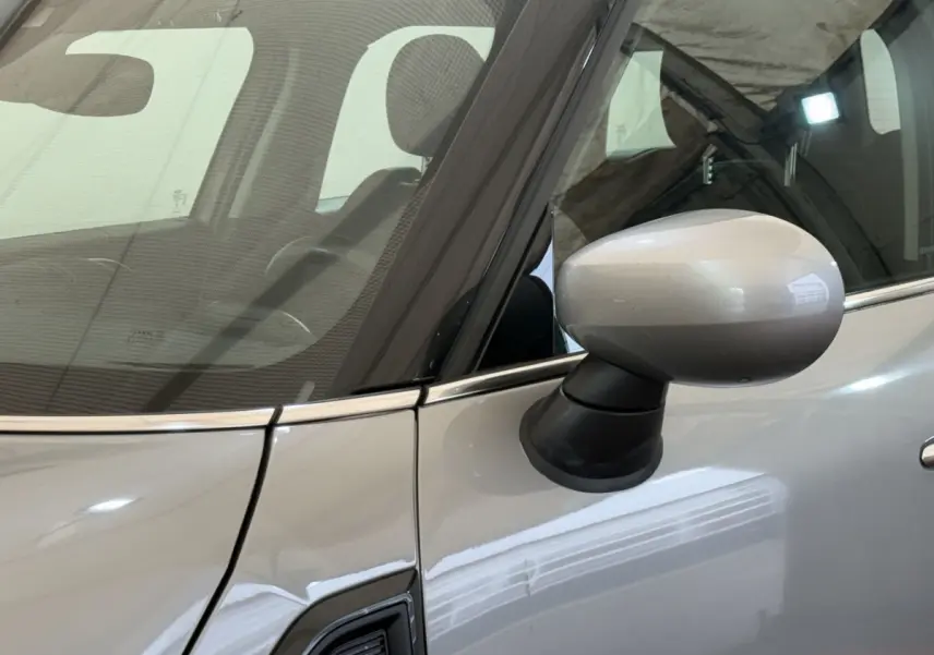 Gros plan sur le rétroviseur côté conducteur d'une MINI Countryman gris clair 2023, avec reflet sur la portière.