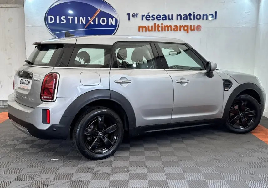 Vue profil droit d'une MINI Countryman Cooper Essential gris clair avec jantes noires et toit blanc en intérieur showroom.