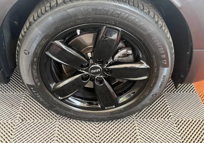 Gros plan sur la roue avant droite du MINI Countryman gris clair, jante noire brillante à cinq branches.