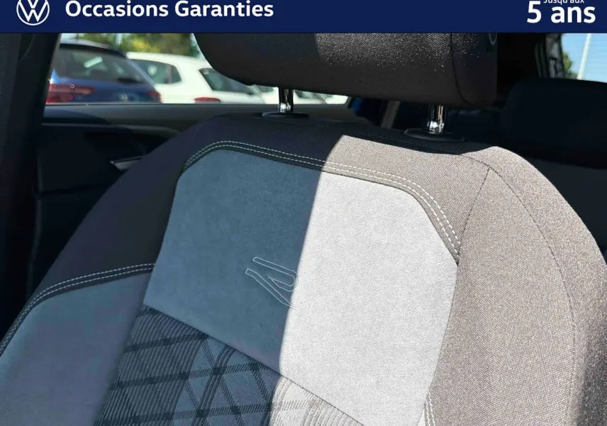 Détail du siège avant en tissu gris avec surpiqûres blanches et logo R embossé, intérieur Volkswagen Taigo 2025.