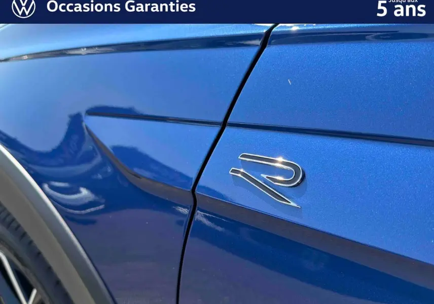 Gros plan sur l'aile avant droite bleue métallisée d'un Volkswagen Taigo avec logo R brillant.