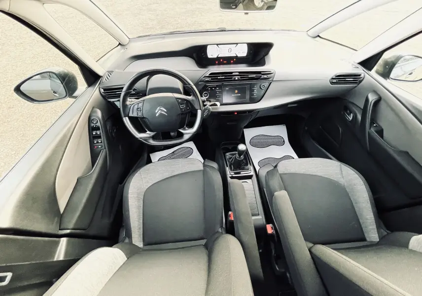 Vue intérieure avant de la Citroën C4 Picasso II avec tableau de bord moderne, volant multifonction et sièges tissu noir et gris.