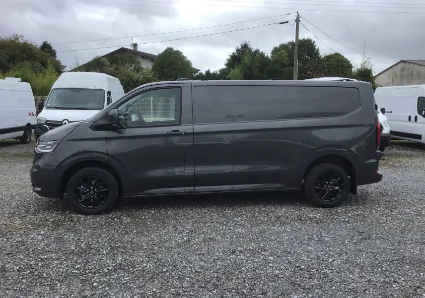 Vue de profil côté gauche d'un Volkswagen Transporter T7 gris anthracite avec jantes noires sur un parking extérieur.