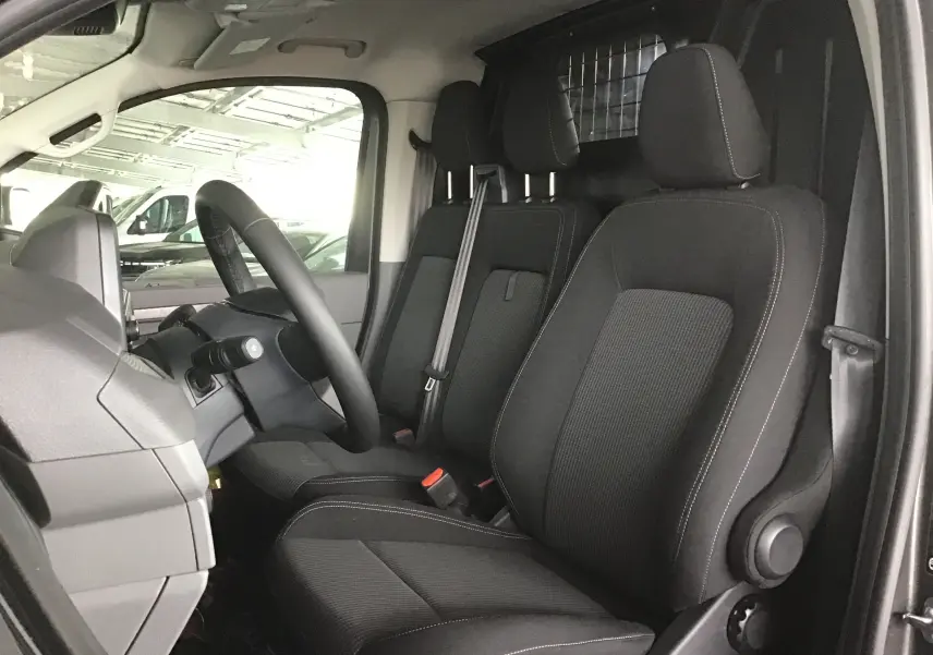 Vue intérieure côté conducteur du Volkswagen Transporter T7 avec sièges noirs et séparation métallique derrière.