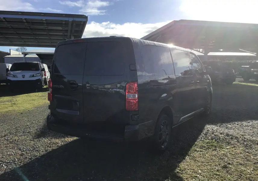Vue 3/4 arrière d'un Citroën Jumpy cabine approfondie gris titane stationné sur un sol gravillonné en extérieur.