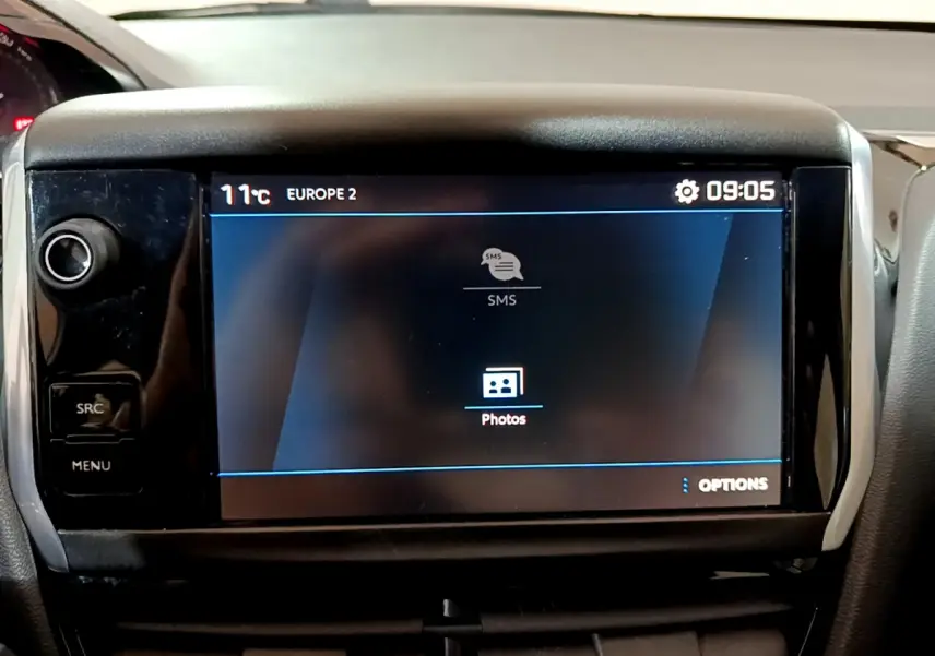 Écran tactile central allumé du tableau de bord d'une Peugeot 208 Puretech 82 Signature, intérieur noir.