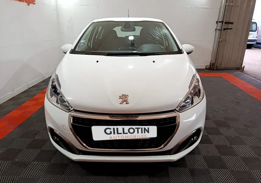Vue frontale d'une Peugeot 208 Puretech 82 Signature blanche avec calandre chromée et phares LED dans un garage.