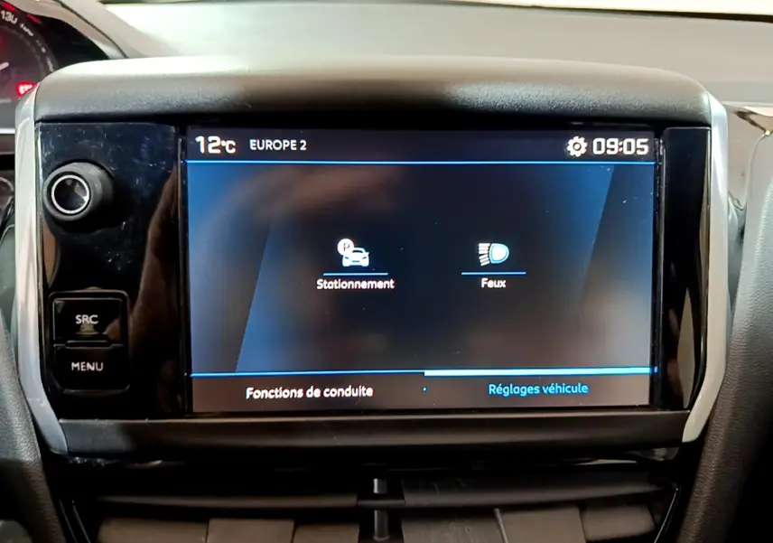 Écran tactile central du tableau de bord de la Peugeot 208 blanche, affichant les réglages de stationnement et feux.