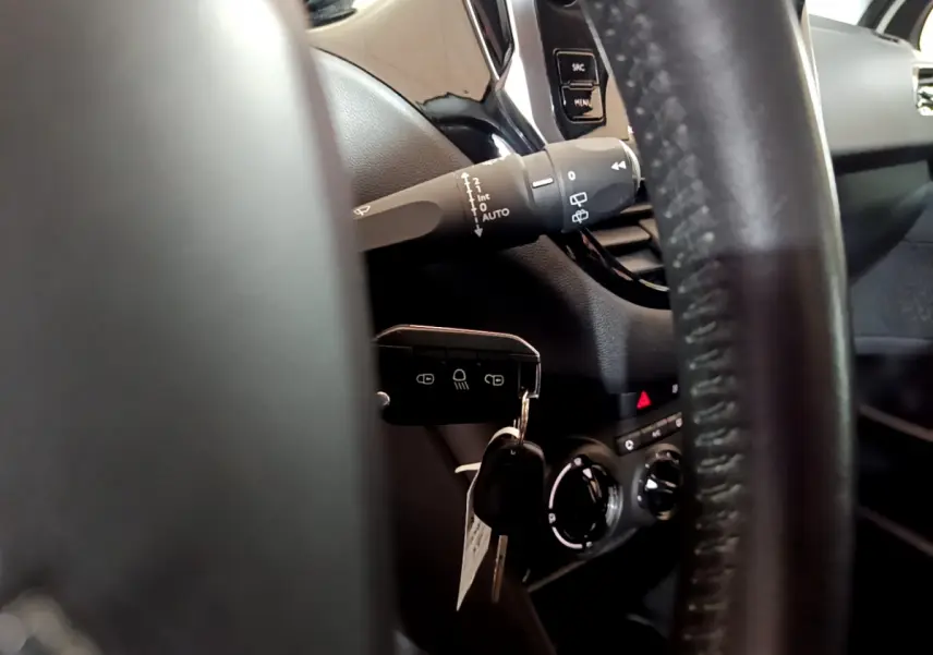Gros plan sur le volant cuir et la clé insérée dans le contacteur d'une Peugeot 208 Puretech 82 Signature, intérieur noir.