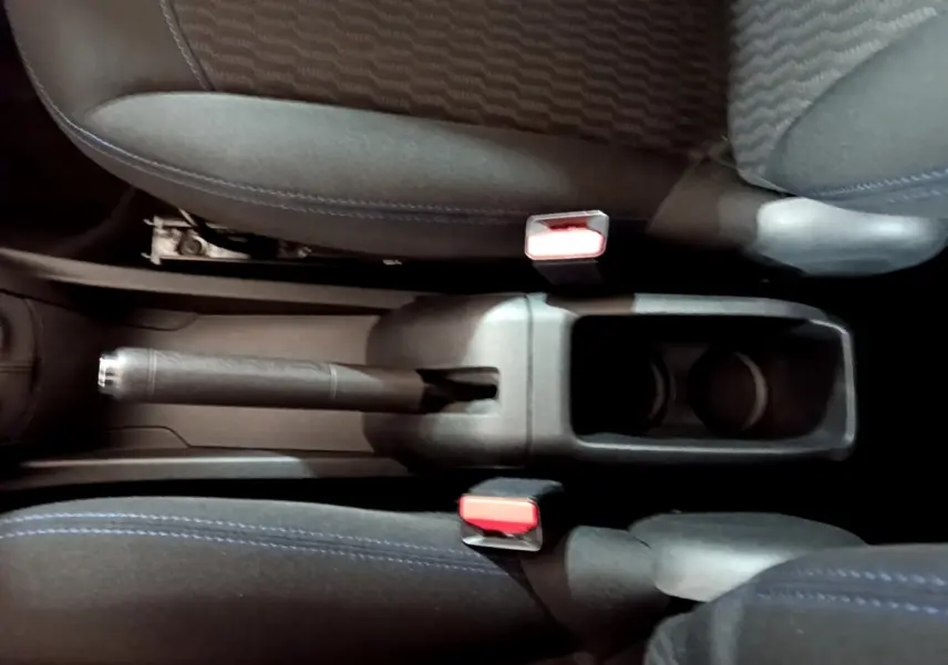 Vue plongeante sur la console centrale noire avec frein à main et porte-gobelets entre les sièges tissu bleu de la Peugeot 208 blanche