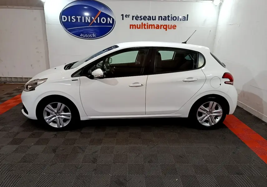 Peugeot 208 Puretech 82 Signature blanc vue de profil côté gauche dans un showroom avec logo Distinxion en arrière-plan.