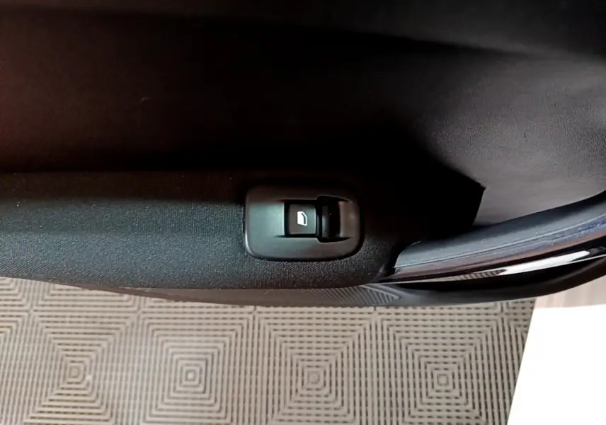 Gros plan sur le bouton de commande de la vitre électrique côté porte intérieure d'une Peugeot 208 blanche de 2018.