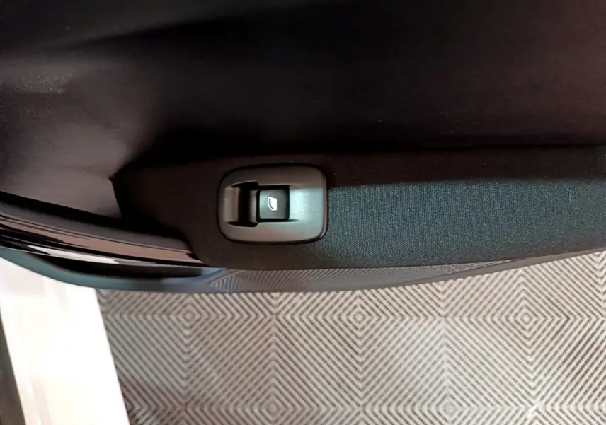 Gros plan sur le bouton de commande de la vitre électrique dans la portière intérieure noire d'une Peugeot 208 blanche.