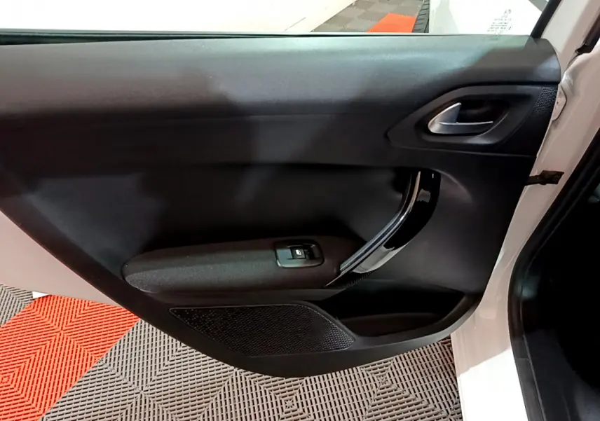 Vue intérieure de la porte côté droit d'une Peugeot 208 blanche avec poignée chromée et commande de vitre électrique.