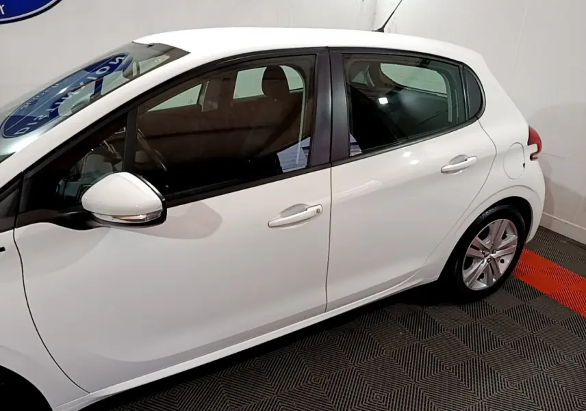 Profil côté gauche d'une Peugeot 208 Puretech 82 Signature blanche, avec rétroviseurs chromés et jantes alliage visibles.