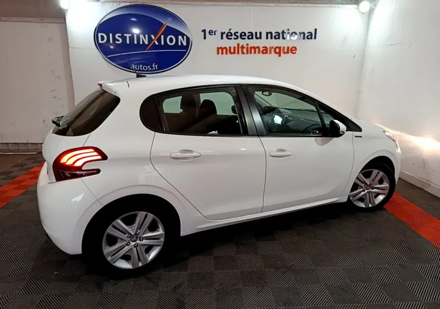 Peugeot 208 Puretech 82 Signature blanc vue de profil côté gauche avec feux arrière allumés en intérieur showroom.