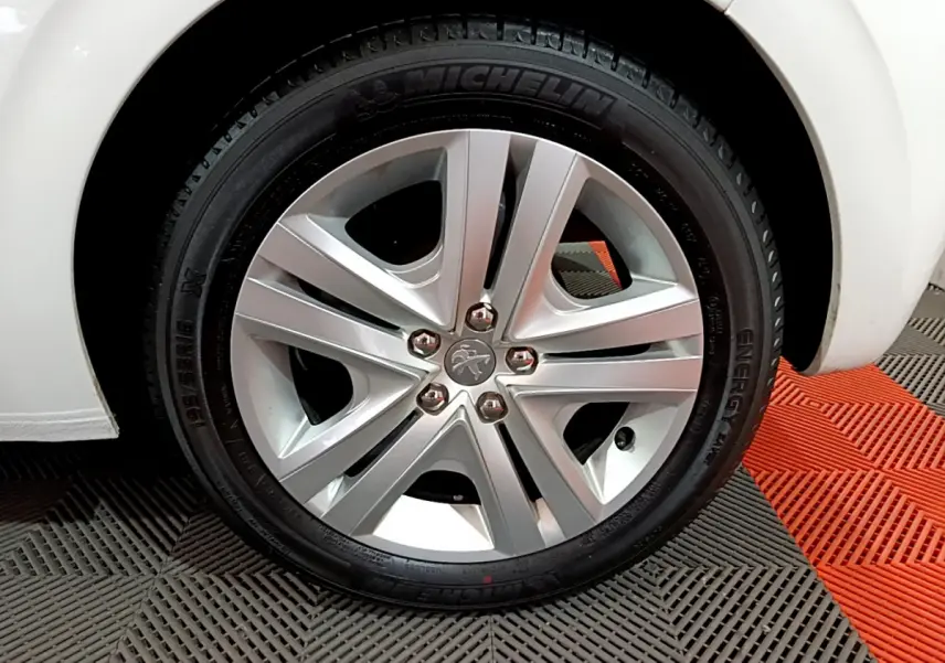 Gros plan sur la roue avant droite d'une Peugeot 208 blanche, mettant en valeur la jante alliage et le pneu Michelin.