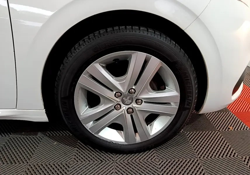 Gros plan sur la roue avant gauche d'une Peugeot 208 blanche, mettant en valeur la jante alliage et le pneu Michelin.