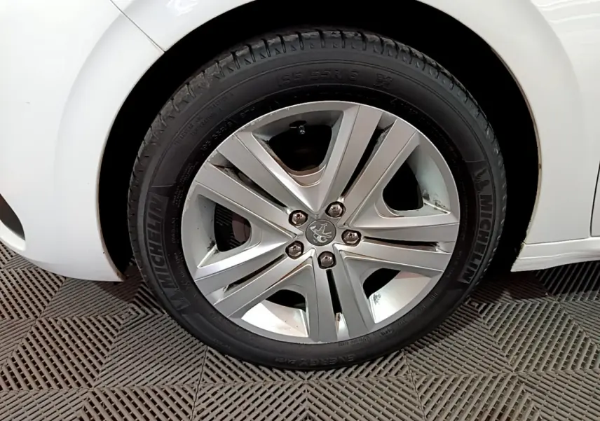 Gros plan sur la roue avant droite d'une Peugeot 208 blanche, mettant en valeur la jante alliage et le pneu Michelin.