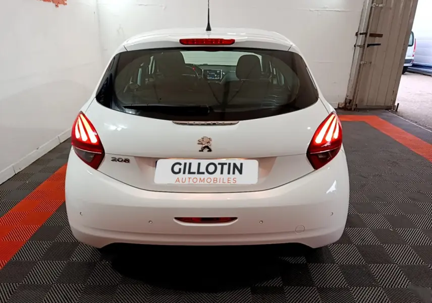Vue arrière d'une Peugeot 208 blanche avec feux arrière allumés dans un garage intérieur.