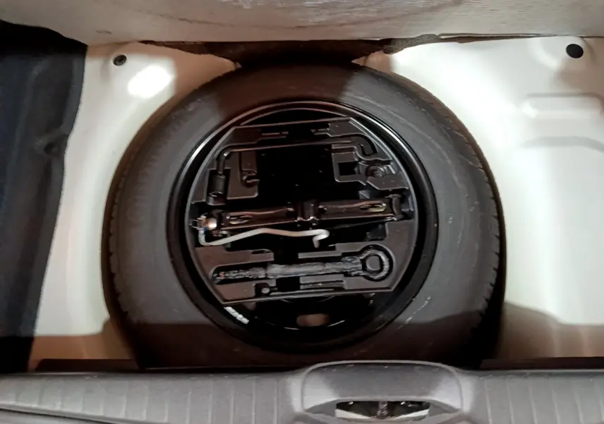 Roue de secours noire avec outils de bord dans le coffre blanc d'une Peugeot 208 Puretech 82 Signature 2018.