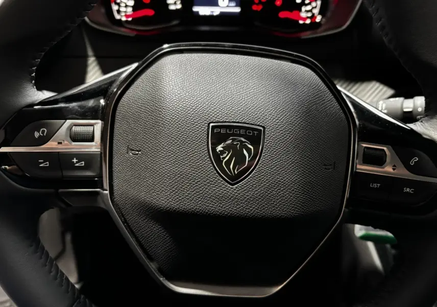 Gros plan sur le volant cuir noir du Peugeot 208 PureTech 100 S&S Active 2024 avec logo lion central et commandes intégrées.