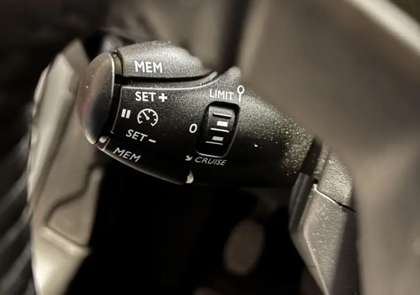 Gros plan sur la commande de régulateur de vitesse noire dans l'habitacle d'une Peugeot 208 gris clair 2024 PureTech Active.