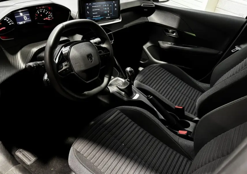 Vue intérieure côté conducteur de la Peugeot 208 PureTech 100 S&S Active 2024, sièges noirs et tableau de bord moderne.