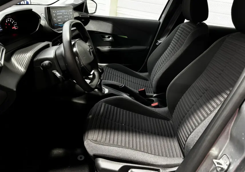 Intérieur avant droit de la Peugeot 208 gris clair 2024, sièges tissu noirs et tableau de bord avec écran tactile.