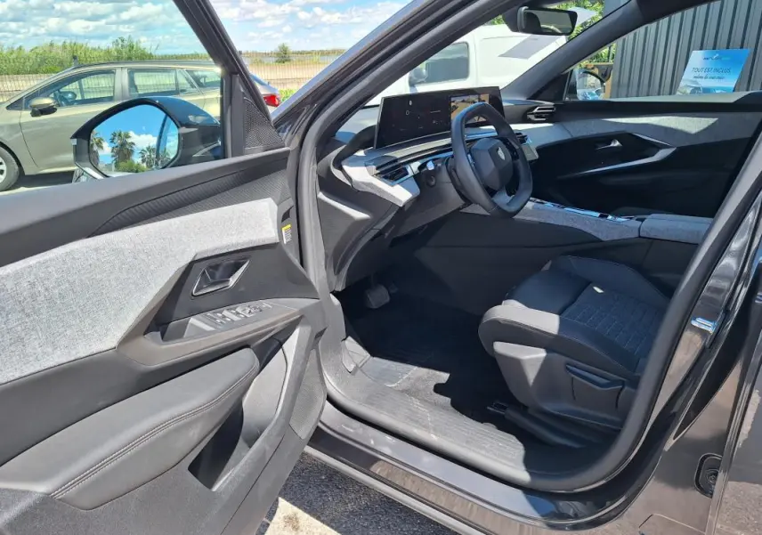 Vue intérieure côté conducteur du Peugeot 3008 Hybrid gris foncé, mettant en valeur le cockpit numérique et les finitions tissu et cuir.