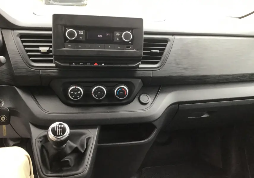 Tableau de bord du Renault Trafic Fourgon blanc 2024, vue intérieure centrée sur la console avec boîte manuelle et commandes clim.