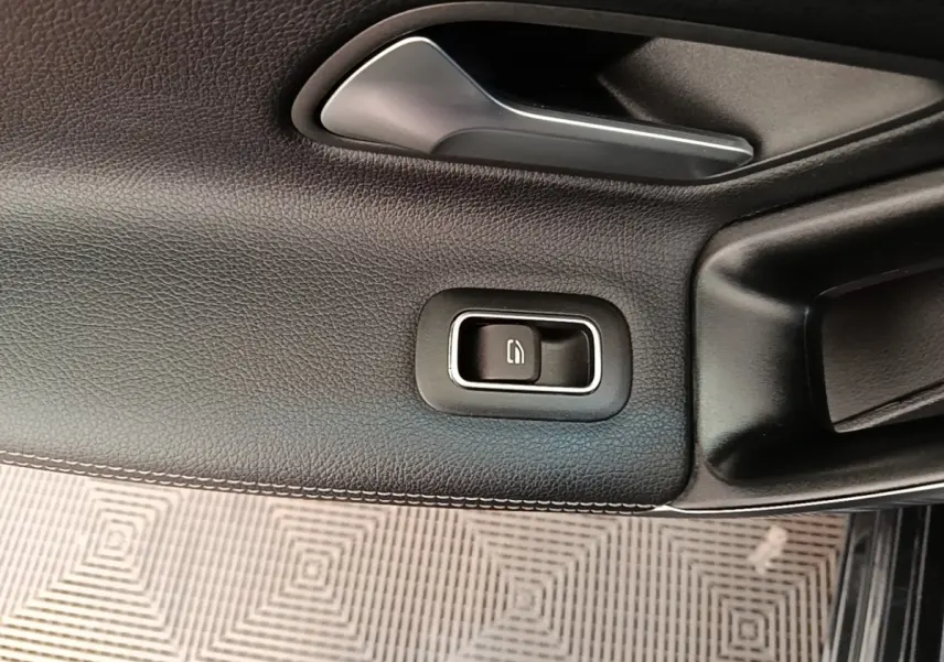 Gros plan sur la commande de la vitre électrique côté conducteur, garniture noire avec surpiqûres blanches.