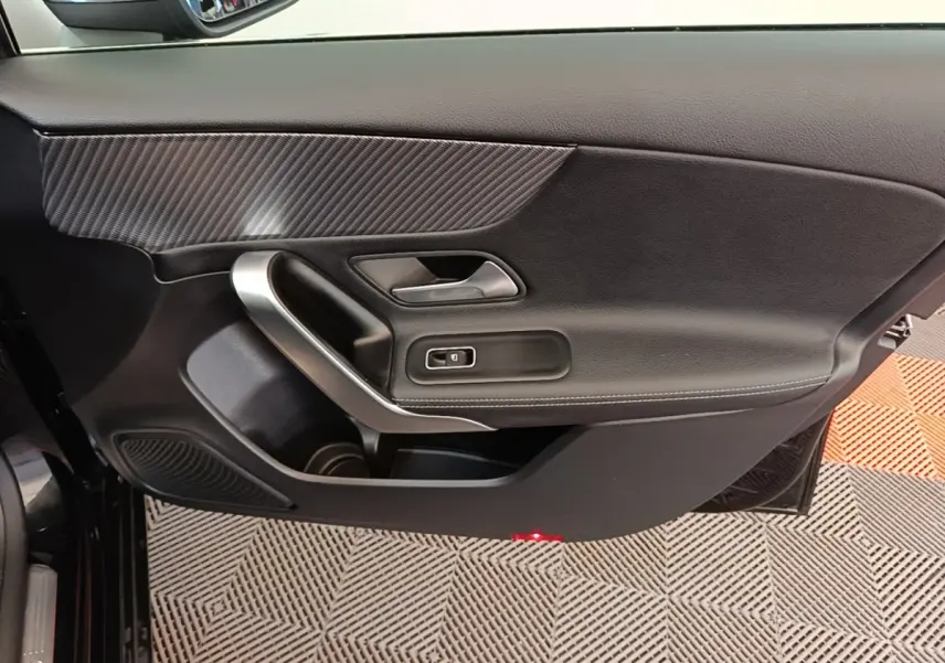 Vue rapprochée de la porte côté conducteur noire de la Mercedes Classe A 250 e Business Line 2023 avec insert carbone et poignée alu.