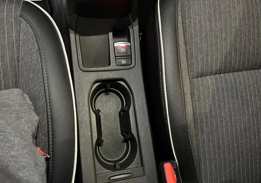 Gros plan sur la console centrale avec porte-gobelets et sièges en tissu noir à surpiqûres blanches de la Renault Clio V.